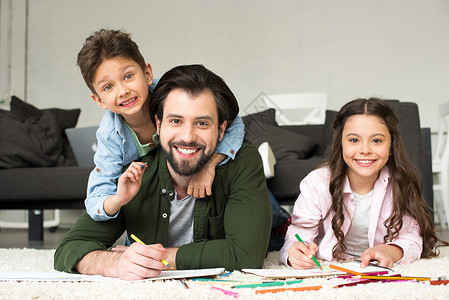 快乐的父亲和可爱的小孩在家里用彩铅笔画时笑着图片