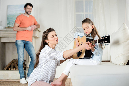 快乐的父亲看着母亲和女儿在家里弹吉他图片