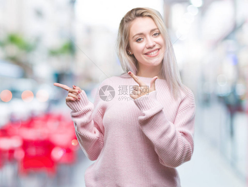 身穿冬毛衣的金发年轻女人带着孤立的背景微笑看着镜头用两只手和指对着图片