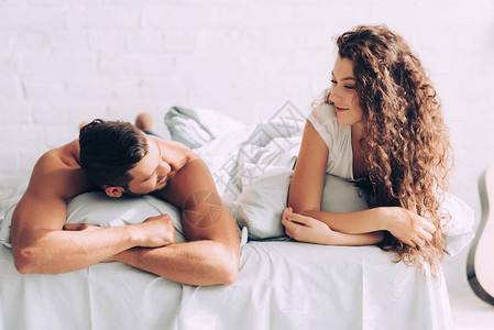 快乐的年轻夫妇说话和躺在床上与枕头图片