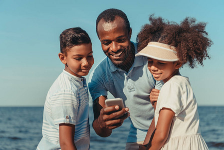 带着可爱的孩子在海边使用智能手机的非洲父亲笑着图片