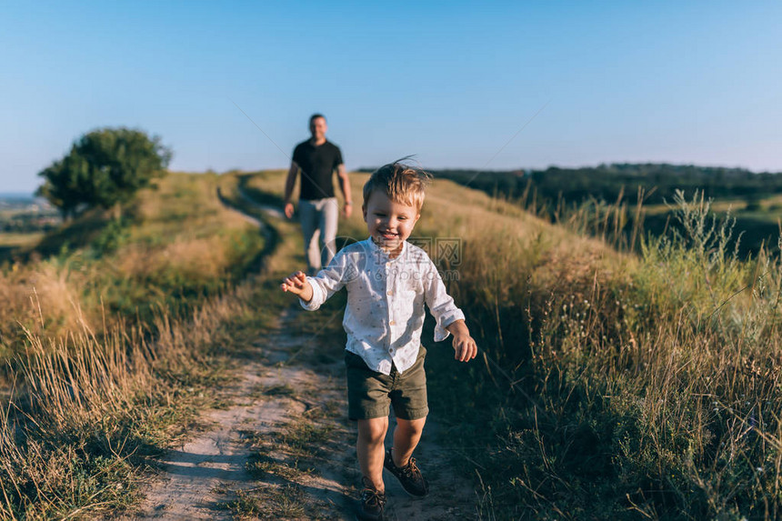 可爱的快乐的小男孩跑在农村路上而父图片