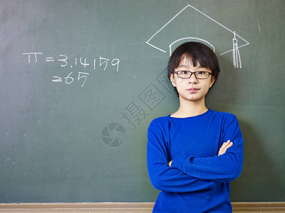 身戴眼镜的亚裔小学男孩站在一个博士帽子下图片