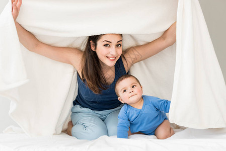 快乐的母亲与她的儿子在白毯子下玩图片