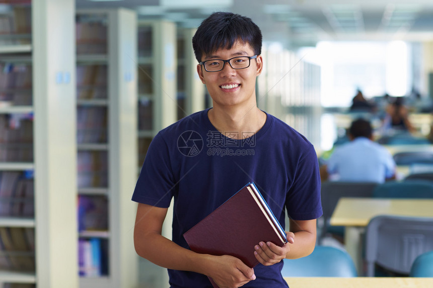 一名年轻男亚洲学生或大学生在图书馆里笑着看图片