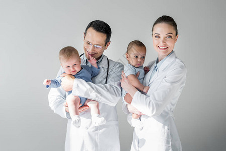 带着小婴儿的成年快乐儿科医生在灰色图片