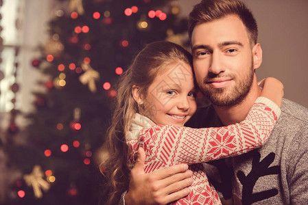 圣诞前夜坐在圣诞树旁微笑的父女拥抱的选择焦点图片