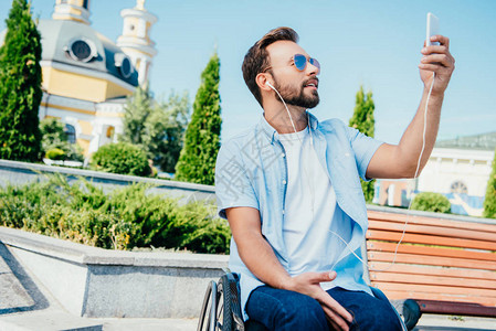 坐在轮椅上帅的男子带着智能手机自拍和图片