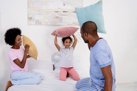 非裔美国父母和女儿在家里床上玩枕图片