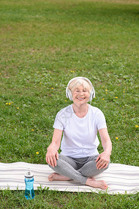 坐在公园瑜伽垫子上用耳机听音乐的图片