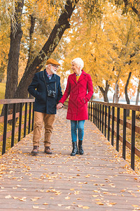 高龄夫妇手握在秋天公园行走时笑图片