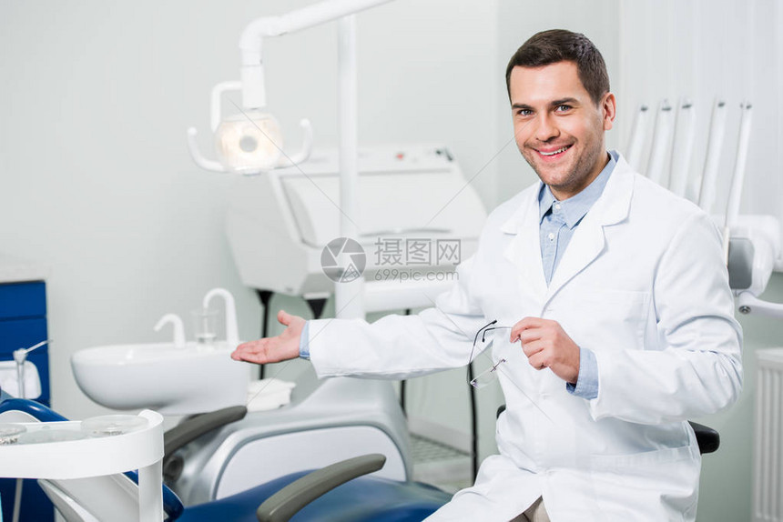 英俊的牙医微笑着在诊所打手势图片