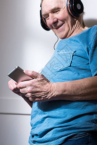 使用智能手机在耳机中微笑的老年图片