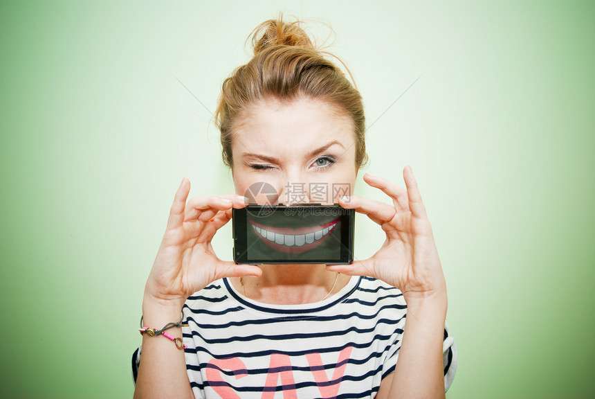 年轻眨眼的女人在嘴上拿着智能手图片