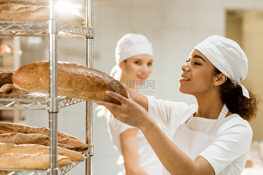 女面包师在烘烤制造时把新鲜面包饼放在架子上图片