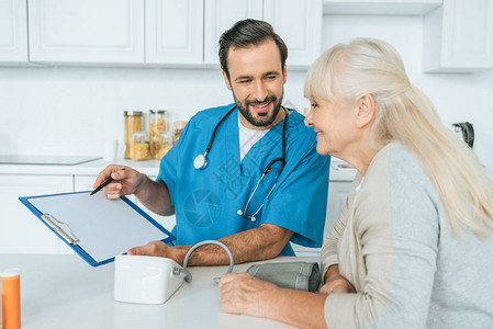 男微笑的护士在测量血压后向快乐的老年妇图片