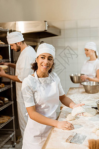 快乐的女面包师在烘焙制造厂揉面团图片