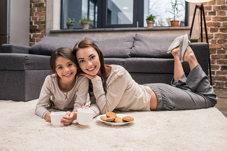 快乐的母亲和女儿在家中喝茶吃饼干时图片