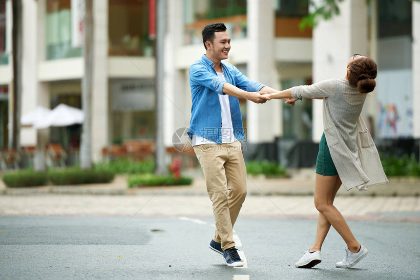 无忧虑的年轻夫妇在街上手牵跳舞笑着微图片