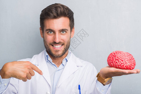 英俊的年轻医生心理学家男子在灰色的格朗基墙上拿着一个大脑图片
