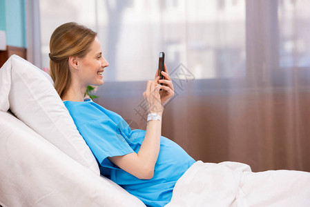 怀孕妇在躺医院床上时使用智能电话但身图片