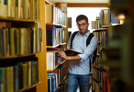图书馆架之间的阿拉伯青年学生阅读书图片
