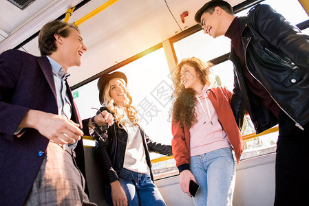 年轻朋友在城市公共汽车上站在一起时微笑交谈的低图片