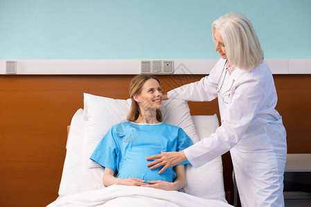 高级医生抚摸躺在医院床上的幸福怀孕妇女肚子图片