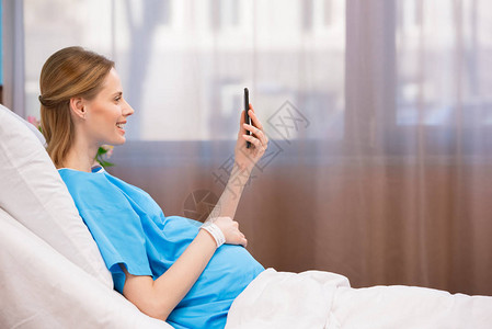 孕妇在躺医院床上时使用智能手机微笑图片
