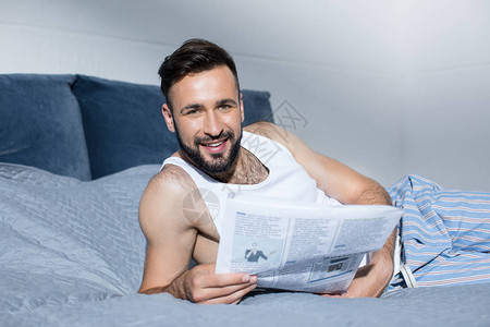长胡子的英俊男子在看报纸躺在床上图片