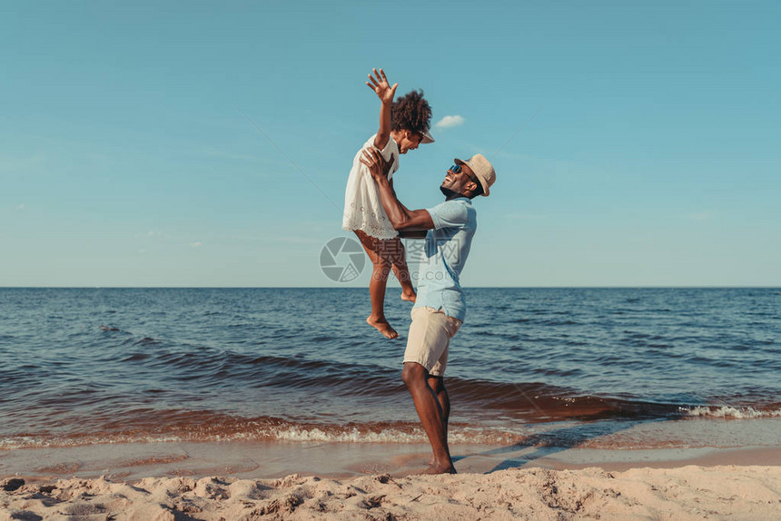 在海滩上和可爱的小女儿玩耍的快乐的非裔美图片