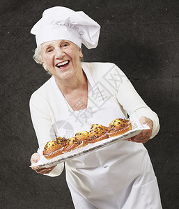 在垃圾背景下拿着松饼托盘的高级女厨师图片