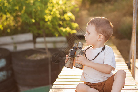 通过双筒望远镜在河岸上看的小男孩的画像可爱的孩子用双筒望远镜坐在河图片