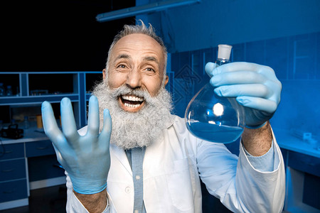 快乐的灰色毛发科学家庆祝成功科学实验并拿着酒瓶图片