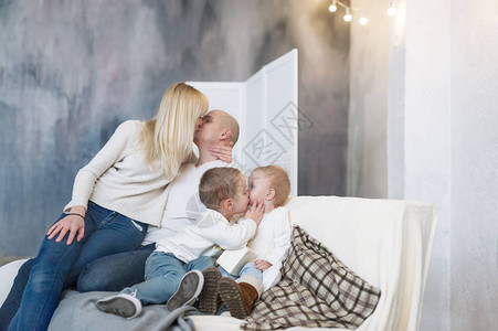 亲吻父母和坐在软沙发上坐在家里的小孩的肖像图片