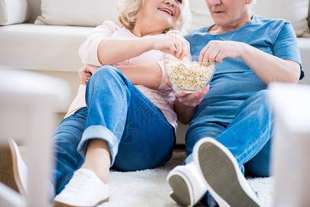 快乐的老夫妇在沙发上吃爆米花的镜头图片