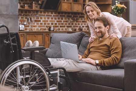 快乐的妇女看着残疾丈夫把双腿放在轮椅上图片
