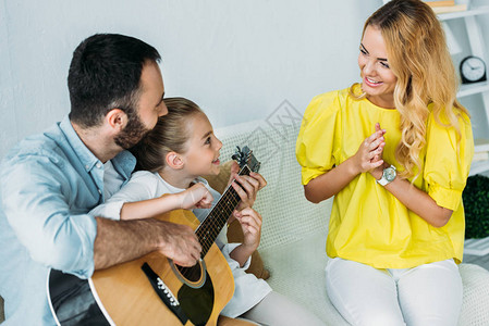 父亲和女儿在家里为母亲打吉他图片
