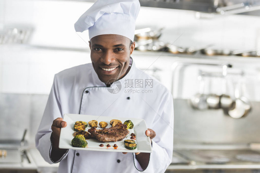快乐的非洲美食厨师拿着餐盘在餐厅厨房吃图片