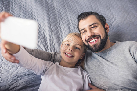 有选择焦点快乐的父亲和小女儿在家里用智能手机自图片