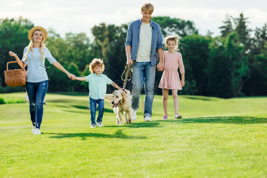 有两个孩子带着猎犬在公园散步的年轻快乐家庭图片