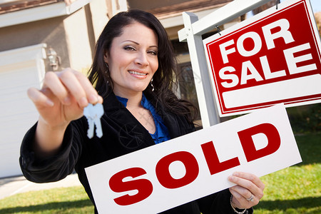 快乐有魅力的西班牙裔女人持有出售房地产标志和钥匙在前面出售房地背景图片
