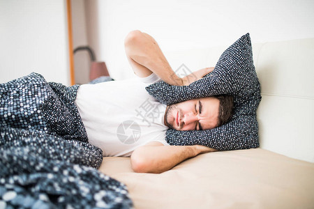 英俊的男人用枕头遮住头和耳朵高清图片