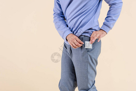 男子将避孕套放入与米色隔离的口袋中的短片图片