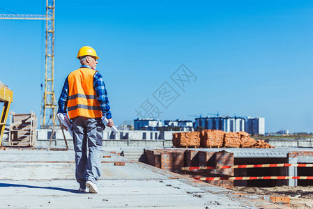 以反射背心和硬帽在建筑工地上行走的建筑工人背景图片