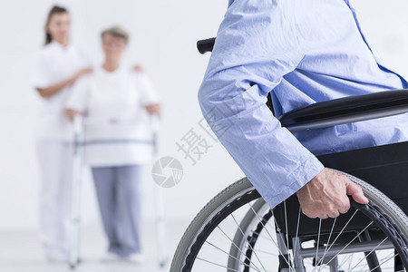 一名使用轮椅的老年男子和一名身背景与护士一起行走的年长妇女图片