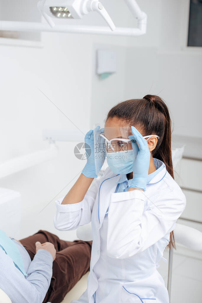 身戴医疗面具的非裔美国牙医在病人图片