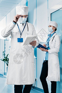 戴着医用口罩的集中男医生调整眼镜和使用数字平板电脑图片