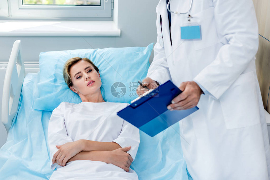 在剪贴板上对医院室女病人指向颈部有听诊器的男医图片