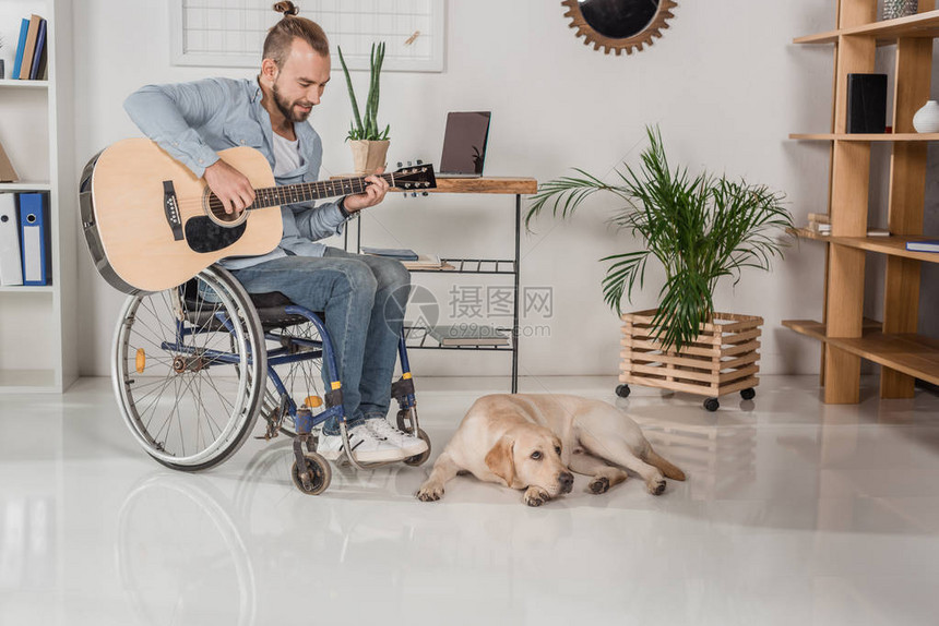 快乐的年轻残疾男子坐在轮椅上弹吉他图片